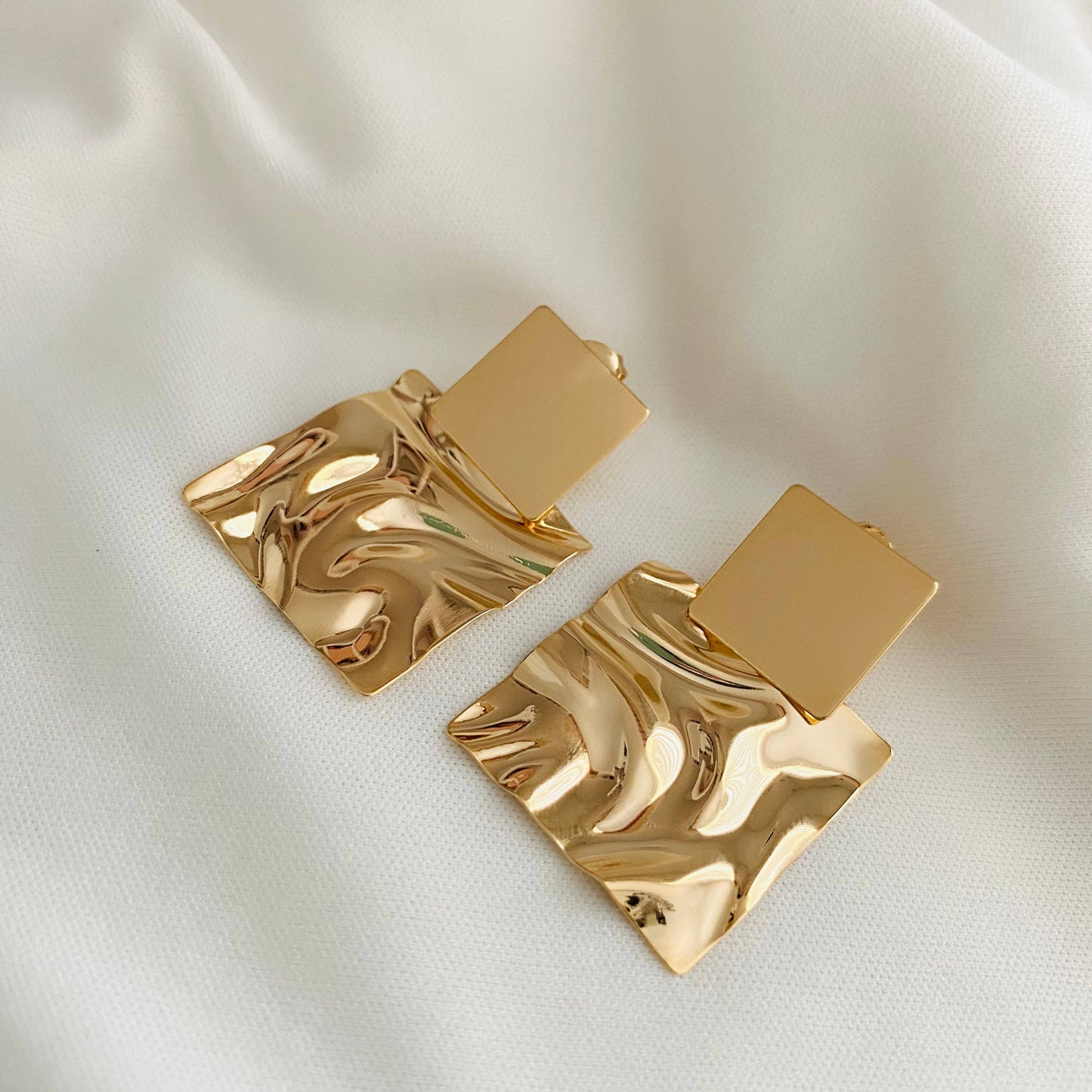 a pair of gold earrings on a white cloth