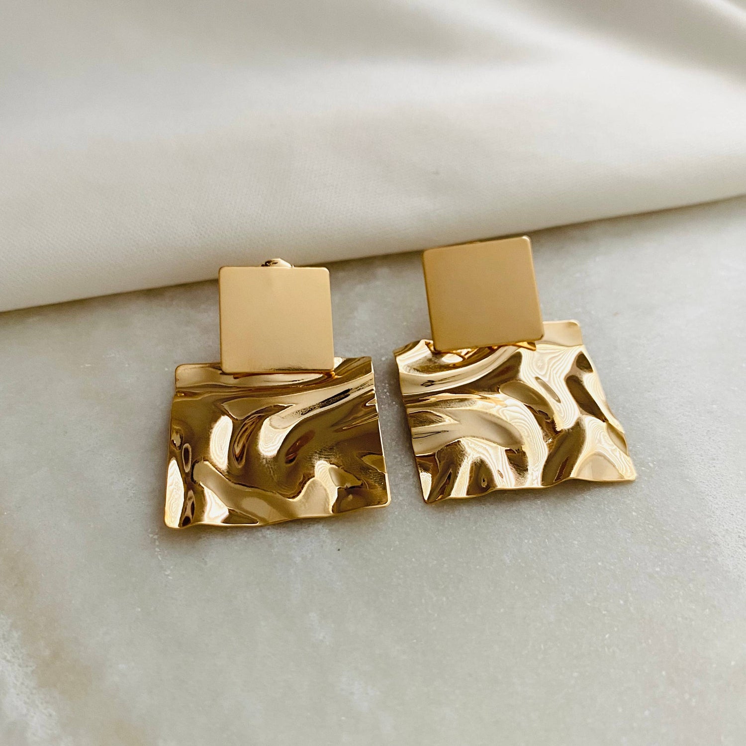 a pair of gold square shaped earrings on a white surface