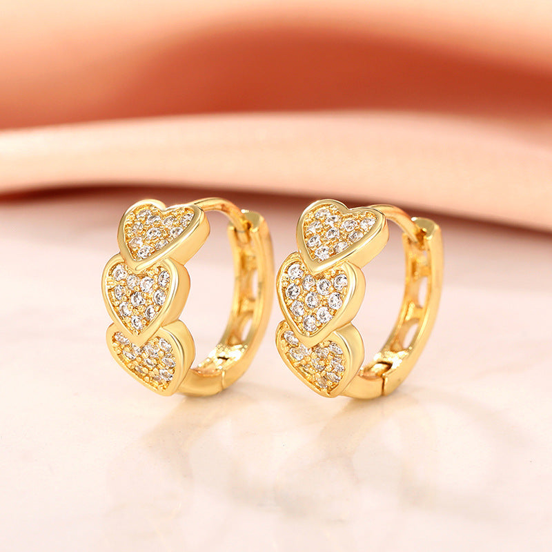 a pair of gold heart earrings on a white surface