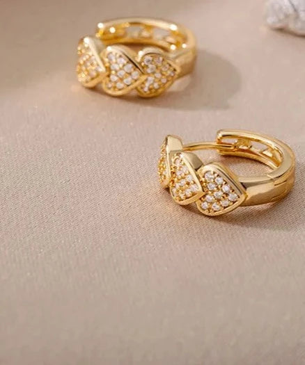 a pair of gold heart earrings sitting on top of a table