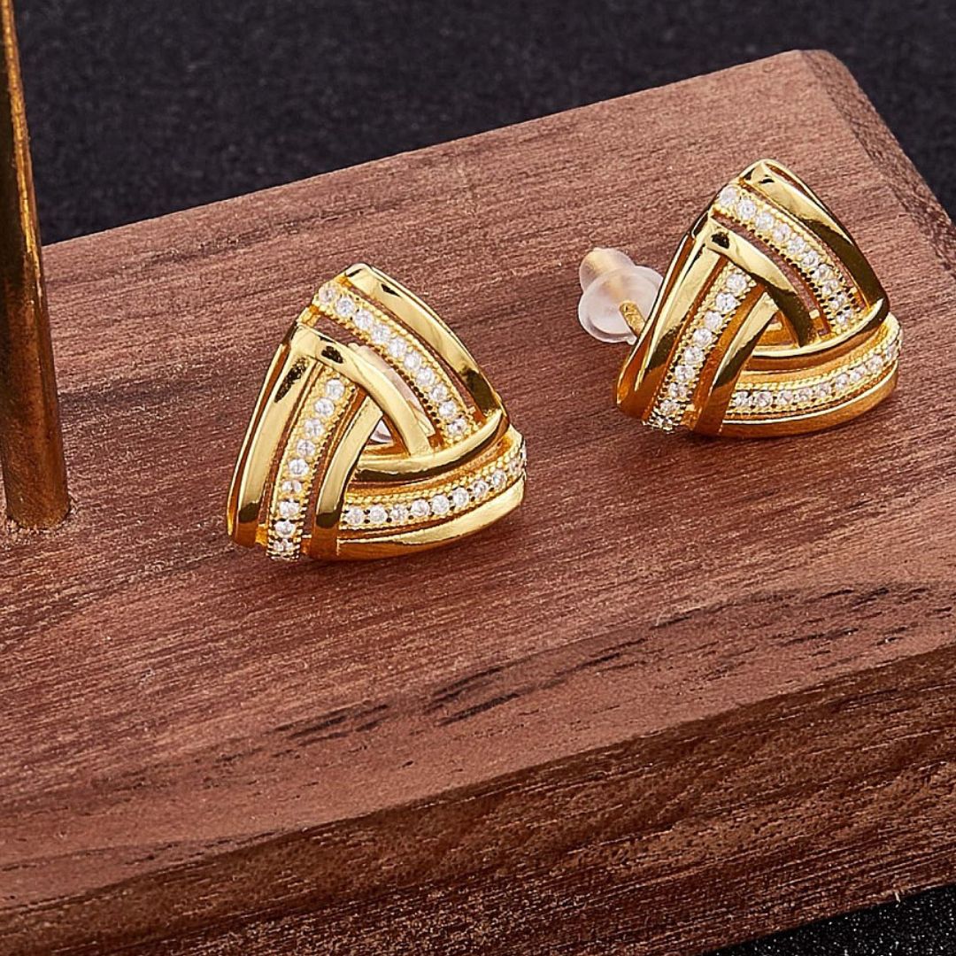a pair of small gold earrings with clear stones on wood