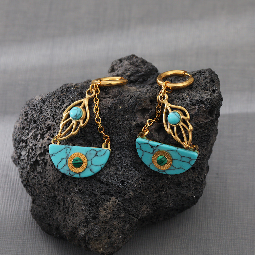 a pair of turquoise and gold earrings on a rock