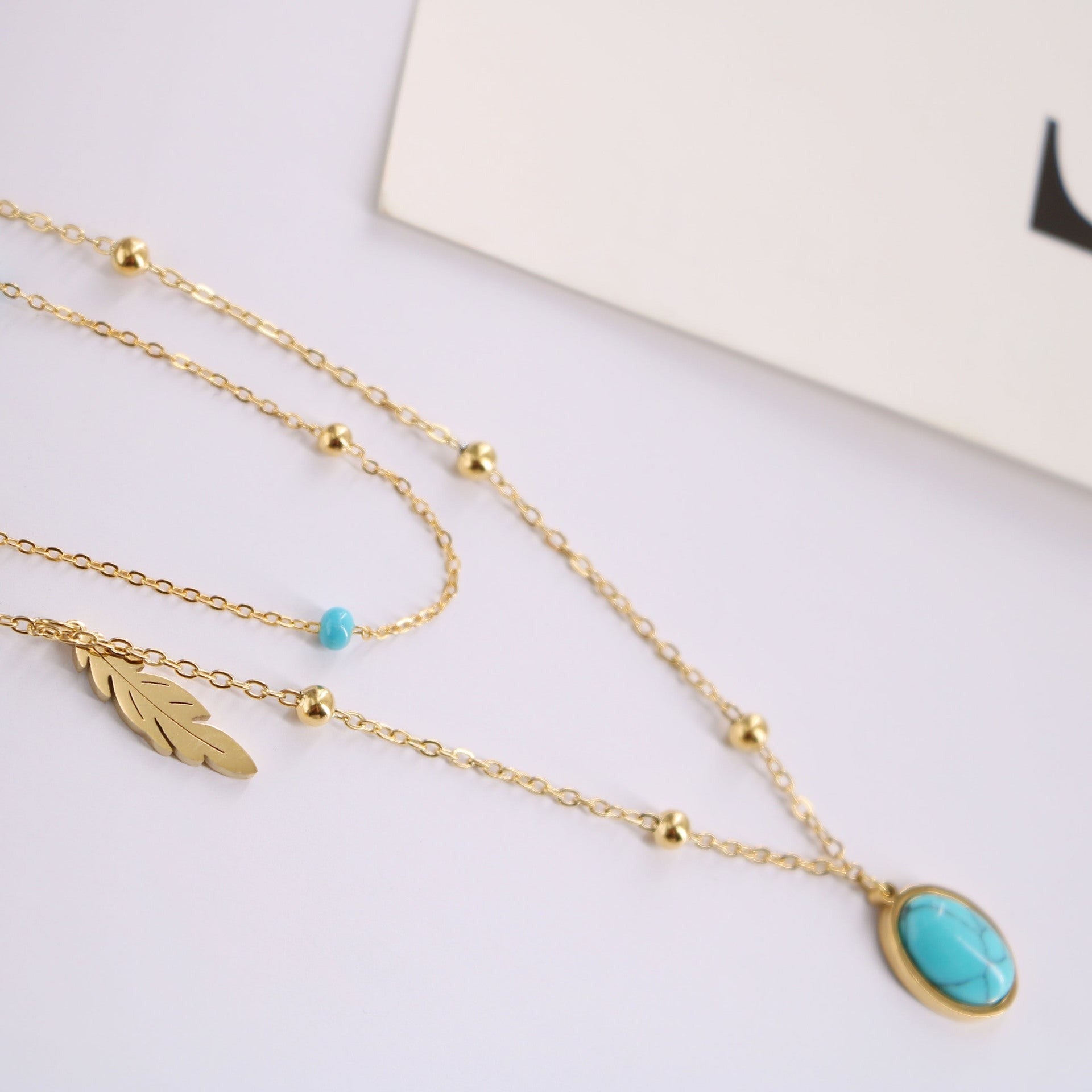 a gold necklace with a turquoise stone and a feather charm